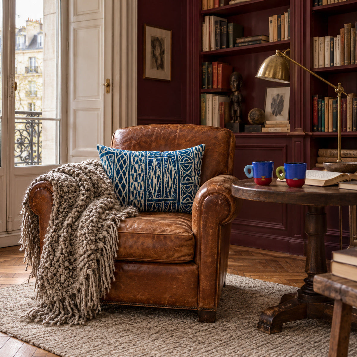 Coin lecture parisien avec coussin FO indigo, plaid TANGGOOR gris chiné et duo de tasses MARABA sur un guéridon.
