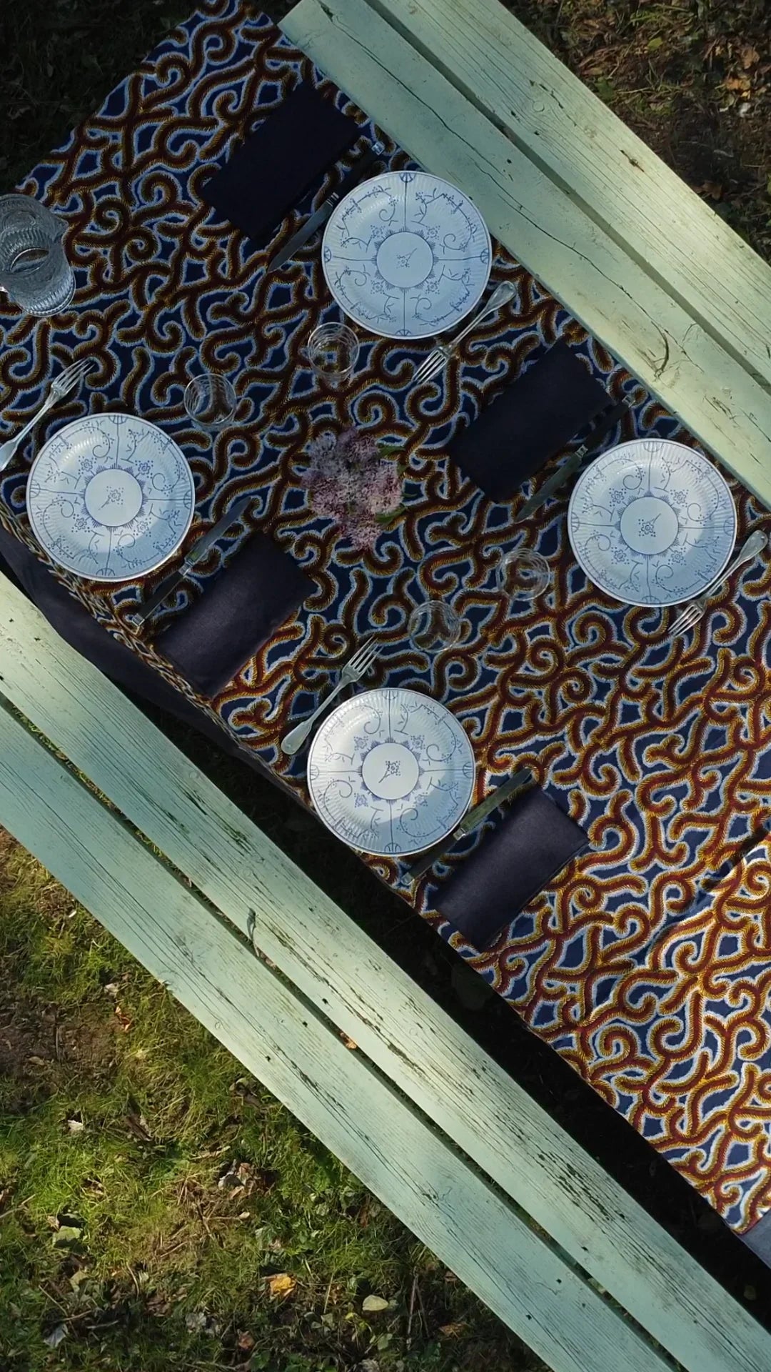 Bovenaanzicht van blauw-oker GIDA-LADHA-tafelkleed op een buitentafel met borden en marineblauwe servetten