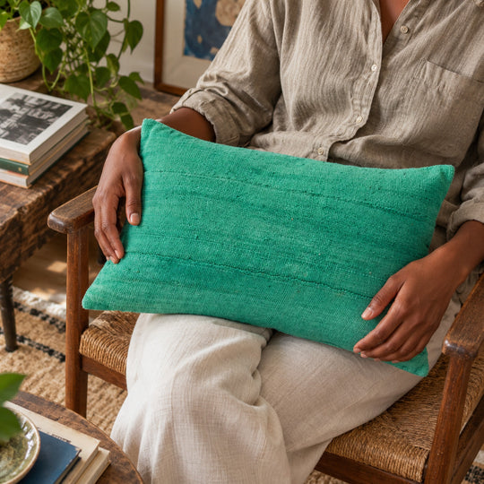 Rechthoekig groen MSINGI kussen op de schoot van een persoon in een houten fauteuil.