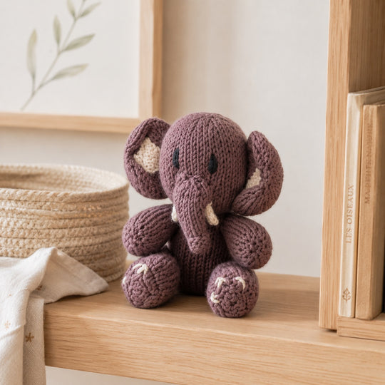 Anatole l’Éléphant – doudou coton bio gris posé sur une étagère en bois avec livres et panier tressé.