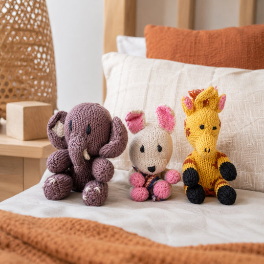 Anatole l’Éléphant, Suzon le Lapin et Léontine la Girafe – trio de doudous coton bio posé sur un lit dans une chambre d’enfant chaleureuse.