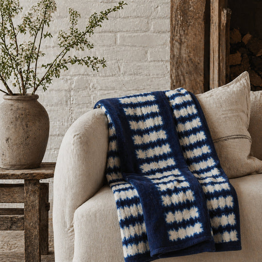 Plaid ZANA-BAHARI en bogolan bleu et blanc par Studio Matongé sur un canapé en lin beige à l'esprit rustique