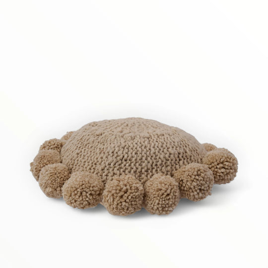 Coussin rond à pompons beige BONBONSI en pure laine mérinos, 30 cm de diamètre. Kenana Knitters pour Studio Matonge. Disponible en 2 tailles (30 cm et 50cm de diamètre) et 3 couleurs (blanc écru, beige et marron foncé). Insert fourni