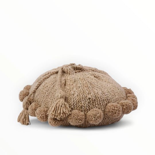 Coussin rond à pompons beige BONBONSI en pure laine mérinos, 50 cm de diamètre. Kenana Knitters pour Studio Matonge. Disponible en 2 tailles (30 cm et 50cm de diamètre) et 3 couleurs (blanc écru, beige et marron foncé). Insert fourni