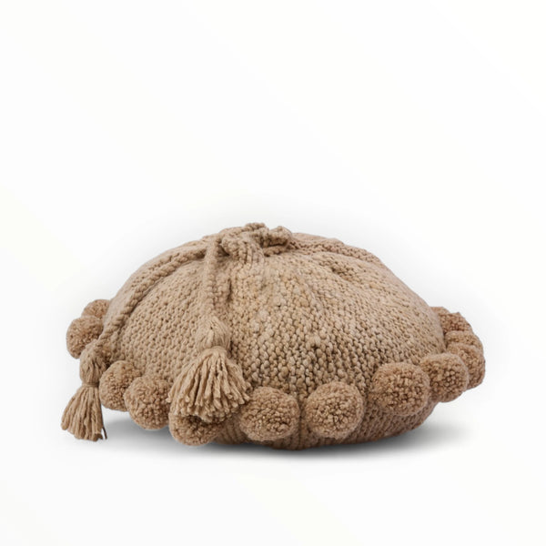 Coussin rond à pompons beige BONBONSI en pure laine mérinos, 50 cm de diamètre. Kenana Knitters pour Studio Matonge. Disponible en 2 tailles (30 cm et 50cm de diamètre) et 3 couleurs (blanc écru, beige et marron foncé). Insert fourni