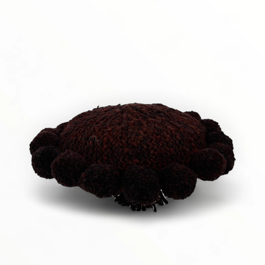 Coussin rond à pompons chocolat BONBONSI en pure laine mérinos, 30 cm de diamètre. Kenana Knitters pour Studio Matonge. Disponible en 2 tailles (30 cm et 50cm de diamètre) et 3 couleurs (blanc écru, beige et marron foncé). Insert fourni