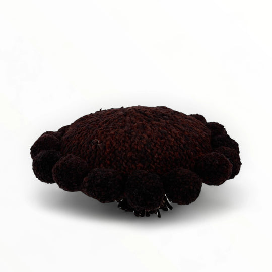 Coussin rond à pompons chocolat BONBONSI en pure laine mérinos, 30 cm de diamètre. Kenana Knitters pour Studio Matonge. Disponible en 2 tailles (30 cm et 50cm de diamètre) et 3 couleurs (blanc écru, beige et marron foncé). Insert fourni