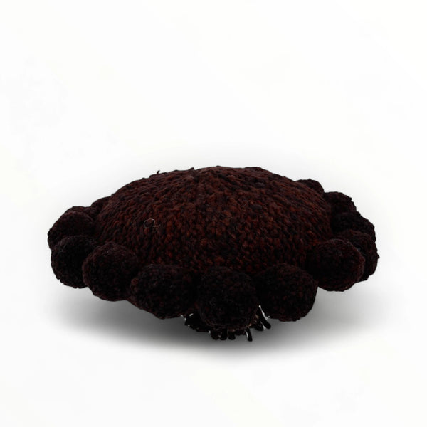 Coussin rond à pompons chocolat BONBONSI en pure laine mérinos, 30 cm de diamètre. Kenana Knitters pour Studio Matonge. Disponible en 2 tailles (30 cm et 50cm de diamètre) et 3 couleurs (blanc écru, beige et marron foncé). Insert fourni
