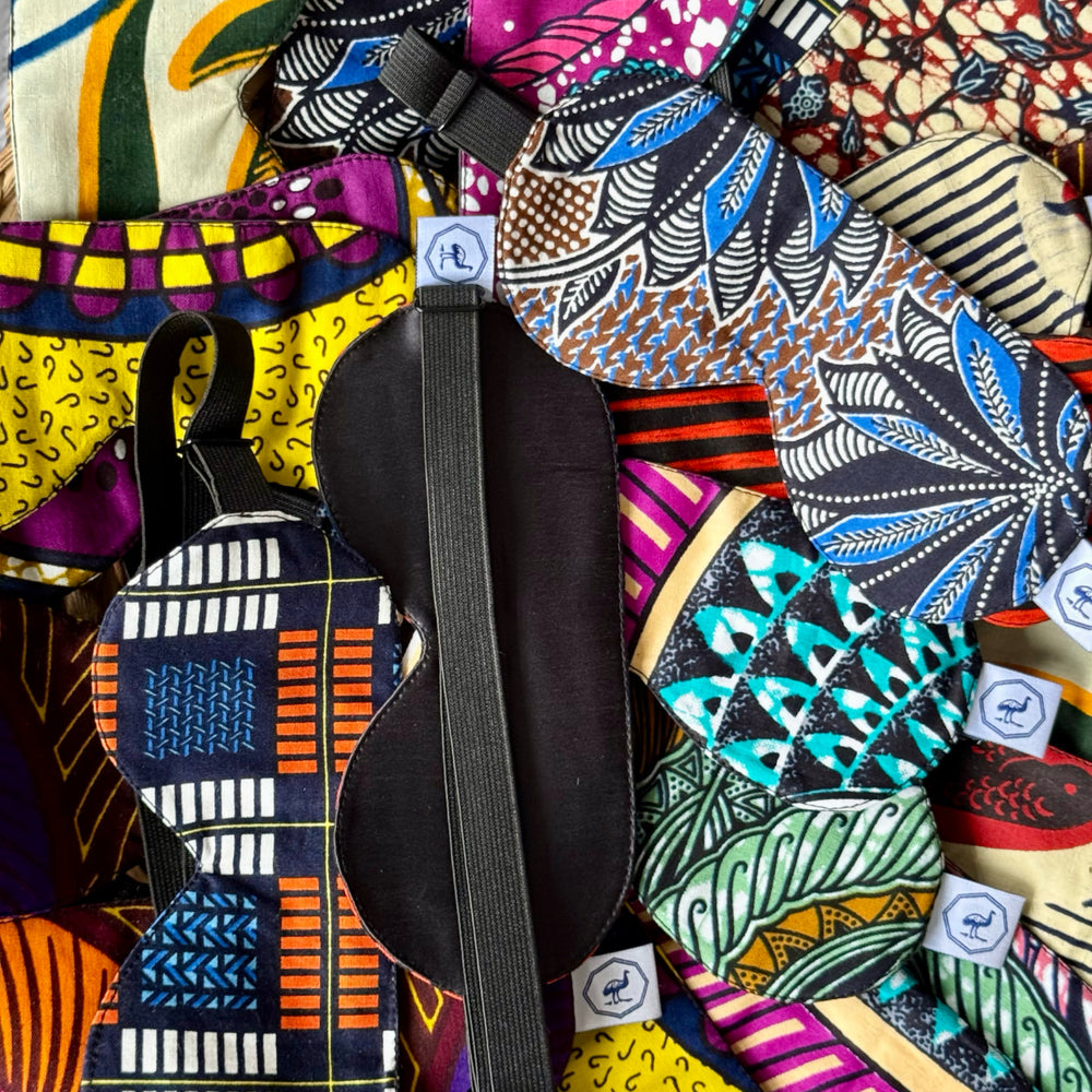 Masques de nuit DARE en wax et soie noire faits main par Studio Matongé, exposés en assortiment coloré – intérieur en soie côté paupières et élastique réglable visibles, confection artisanale en Belgique avec chutes de tissu upcyclées.