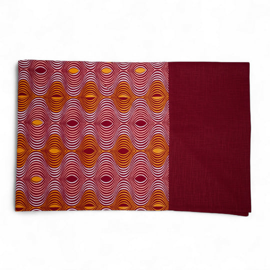Nappe GIDA_ZUBA pliée sur fond blanc. Bord en lin bordeaux et centre en wax bordeaux, abricot, rose dragée et blanc.
Ici rectangulaire : 158 x 250 cm. Existe aussi en format carré 130 x 130 cm.
A assortir avec nos serviettes AYO ou SAVUTI.