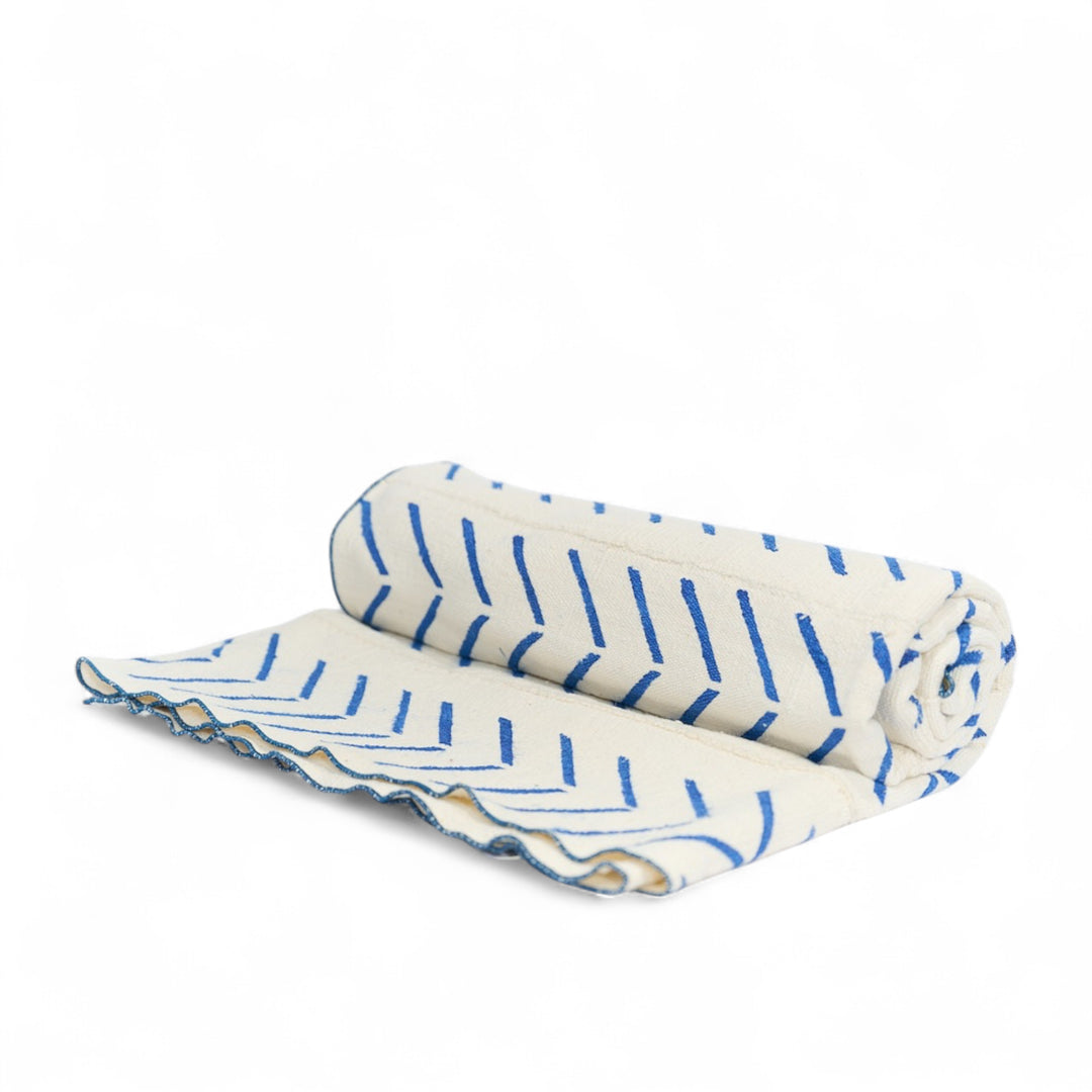 Plaid FEMI-OKUN en bogolan blanc à motifs bleus en forme de flèches stylisées. Tissé et orné à la main au Mali. Finition au point de bourdon coordonné réalisée artisanalement en Belgique