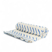 Plaid FEMI-OKUN en bogolan blanc à motifs bleus en forme de flèches stylisées. Tissé et orné à la main au Mali. Finition au point de bourdon coordonné réalisée artisanalement en Belgique
