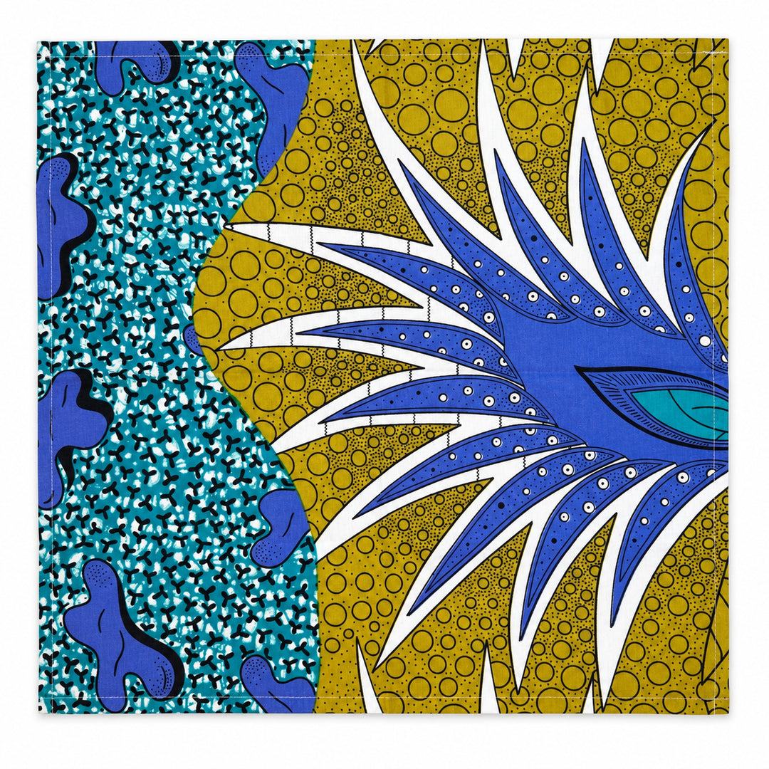 Serviette de table AYO-LAGA dépliée sur fond blanc, avec son motif turquoise, jaune olive, bleu outremer, blanc et noir.
Les proportions de couleurs et placement des motifs varient d'une pièce à l'autre selon la coupe dans le tissu. 