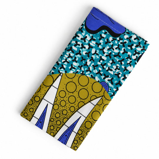Serviette de table AYO-LAGA pliée sur fond blanc, avec motifs turquoise, jaune olive et bleu outremer.