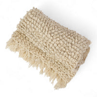Zusammengelegte TANGGOOR Decke aus ecrufarbener Wolle mit großen Strickschlingen und Fransen, in Kenia handgestrickt.