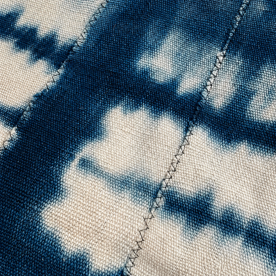 Détail de la matière pour le plaid ZANA-BAHARI tie and dye en coton bleu indigo et crème, filé tissé et teint à la main au Mali, doublé de double gaze de coton marine. Confection réalisée en Belgique dans des ateliers protégés.