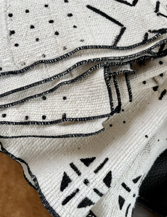 Détails des plaids LENGO et MSALABA en bogolan de coton bio écru avec des motifs noirs. Nos plaids, filés, tissés et teints au Mali dans la région de San sont bordés au point de bourdon en Belgique.  