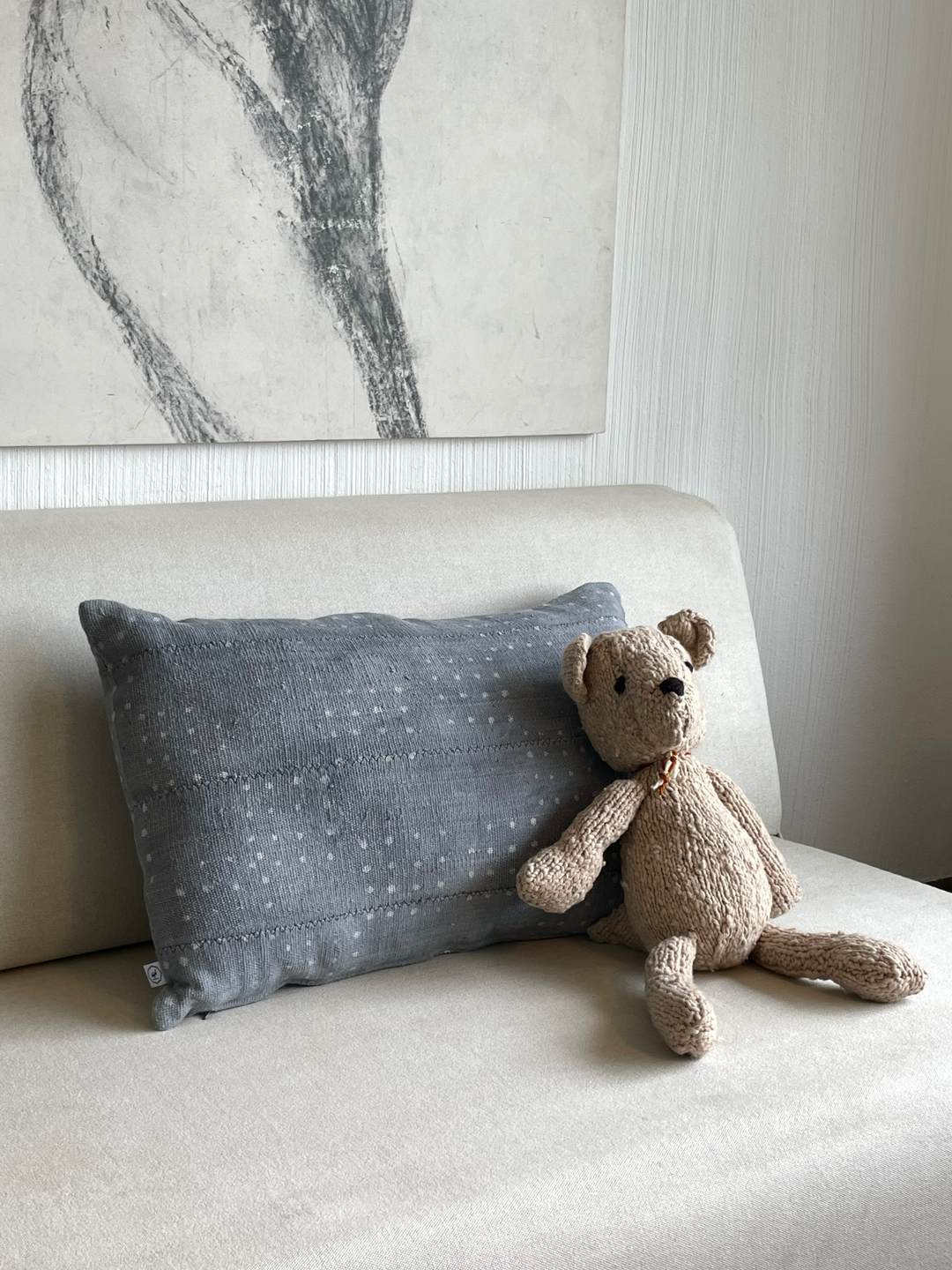Sur le sofa, notre doudou ours MICHEL en pure laine mérinos confortablement installé sur notre coussin bogolan gris KIJIVU en coton bio et teinture naturelle. 