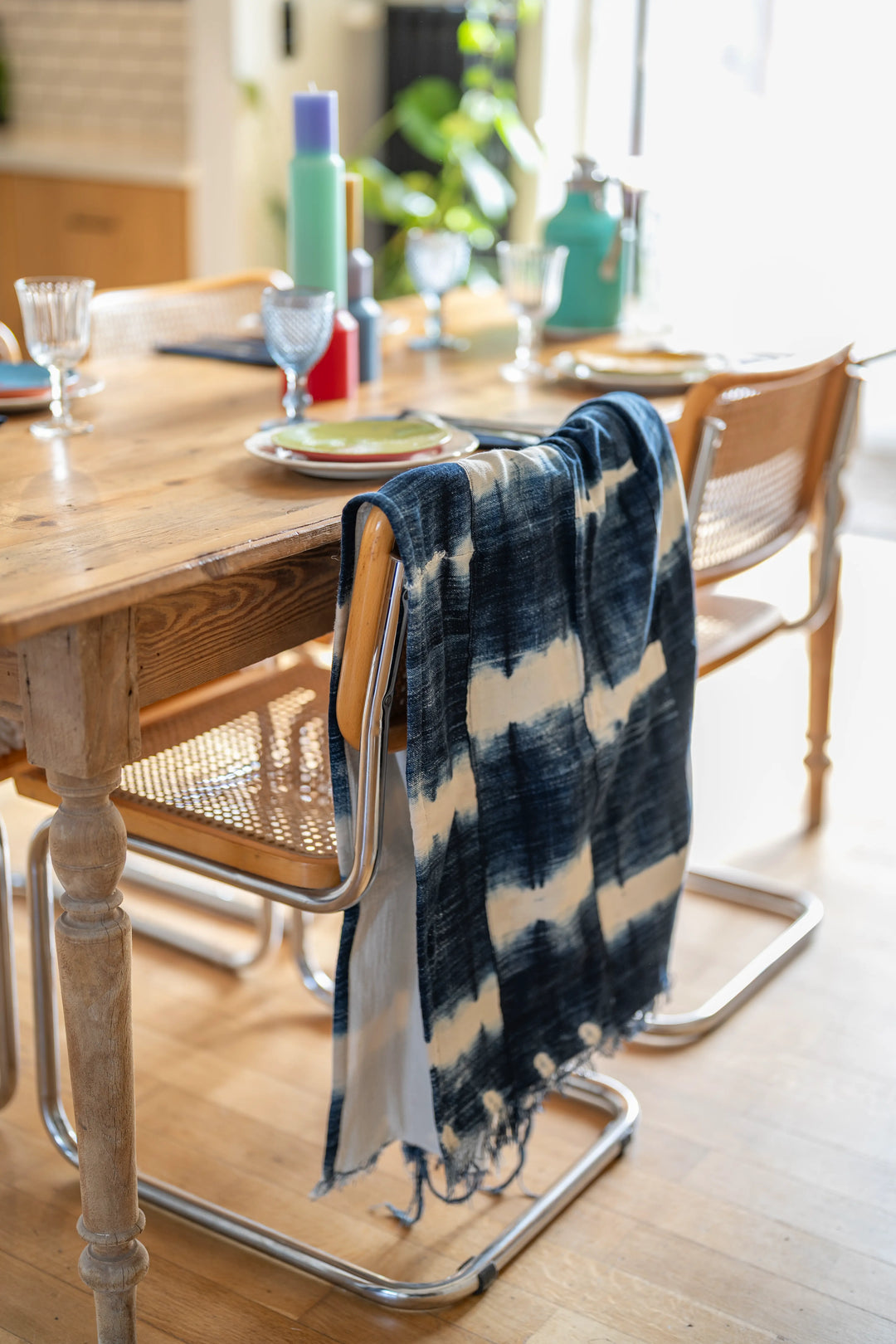 Plaid OKAN en coton artisanal indigo et gaze de coton, accroché à une chaise autour d'une table dressée, déco conviviale.