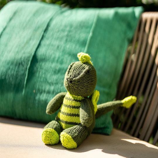 ELIOT, le doudou dragon de Studio Matongé prend un bain de soleil confortablement installé au jardin sur le coussin MSINGI en bogolan de coton bio.  