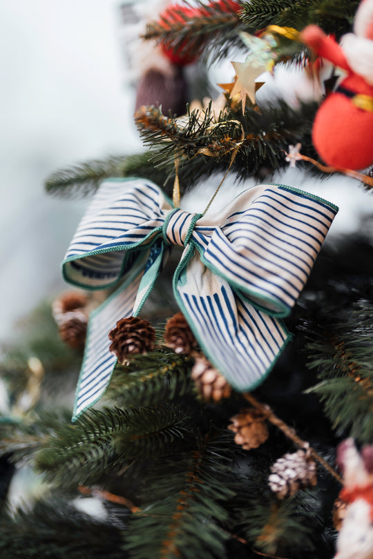 Dans le sapin, nœud décoratif de Noël ZAWADI en wax MTOTO blanc à rayures bleues et motifs verts, fabriqué à la main à partir de chutes de tissu, Studio Matongé.