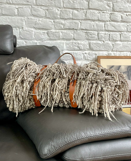 Le porte plaid TITI, fait main est lefruit de la collaboration entre Studio Matongé et les ateliers Larfeuille à Paris. En cuir cognac, il maintient élégamment le plaid TANGGOOR gris chiné en pure laine, tricoté main par les femmes artisans de la coopérative Kenana-Knitters au Kenya.