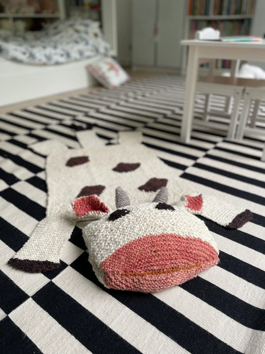 Dans une chambre d'enfant à l'esprit graphique, le tapis vache MOOSHY, tricoté main en pure laine. Super amusante avec sa grosse tête rembourrée propice à la lecture ou à la rêverie de nos kids.