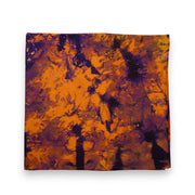 Nappe DUNDA – AMBER NIGHTS en kokodunda, pliée, motif abstrait aux nuances d’ocre, ambre et violet profond, vue de dessus sur fond blanc.