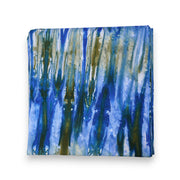 Nappe DUNDA-LAGUNE en kokodunda, pliée, motif abstrait aux nuances de bleu, vert lagune et écru, vue de dessus sur fond blanc.