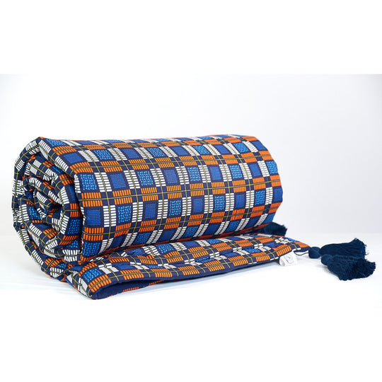 Couvre-pieds KULALA par Studio Matongé en wax de coton écossais bleu, blanc et orange. Notre couvre-pieds est doublé d'une douillette double gaze et rehaussé d'élégants pompons de coton marine.
Dimensions 110 x 220 cm environ.  
