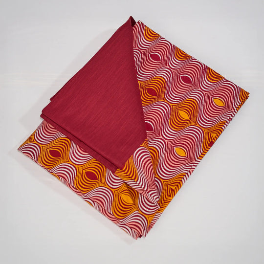 Nappe GIDA_ZUBA pliée sur fond blanc. Bord en lin bordeaux et centre en wax bordeaux, abricot, rose dragée et blanc.