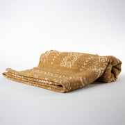 Plaid en bogolan de coton ocre ARDHI. Motifs ethniques écrus. En coton bio filé, tissé, teint et décoré à la main par nos artisans dans la région de Ségou au Mali. Approximativement 153 x 117 cm.
