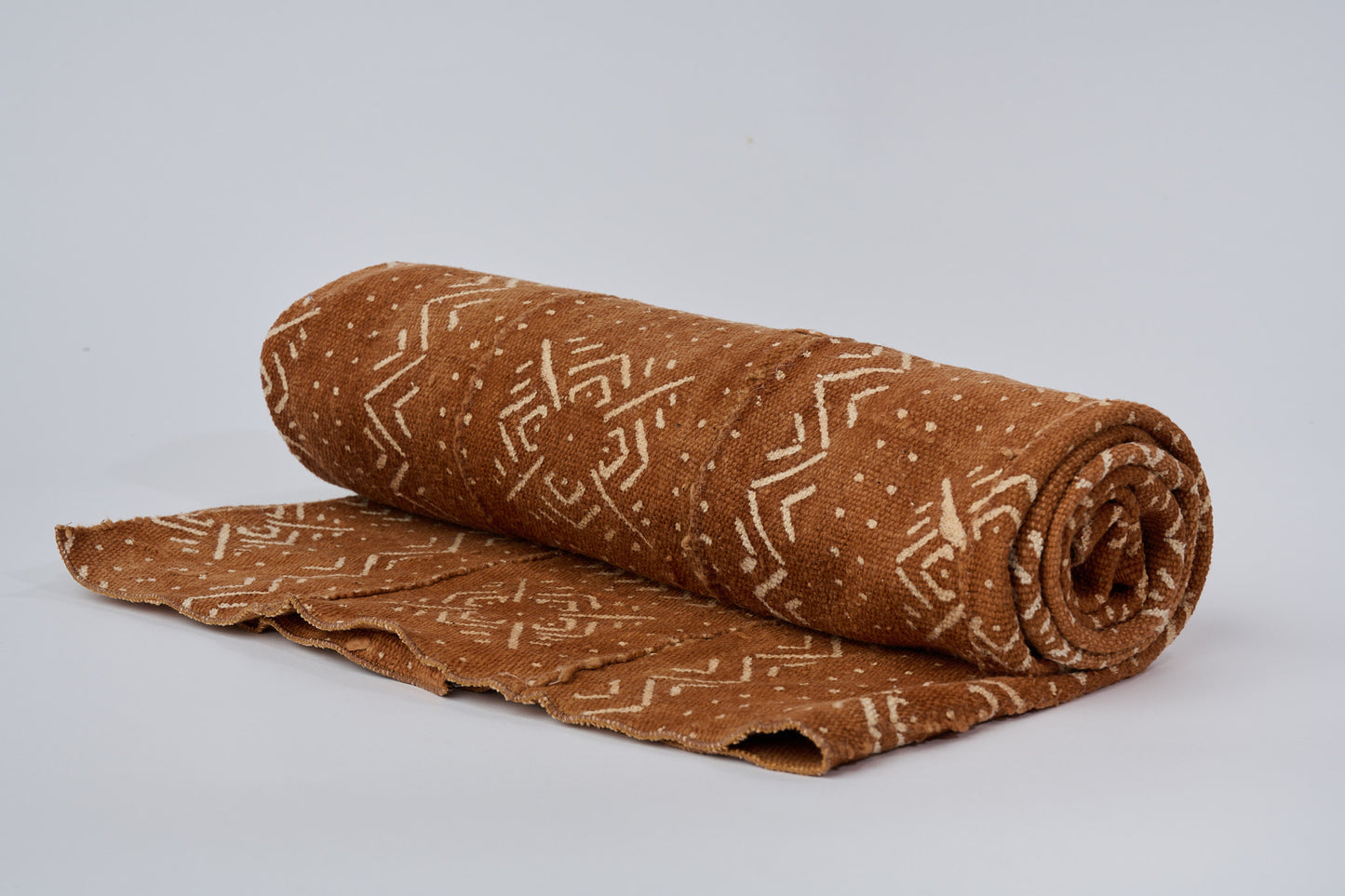 Plaid en bogolan de coton terracotta ARDHI. Motifs ethniques écrus. En coton bio filé, tissé, teint et décoré à la main par nos artisans dans la région de Ségou au Mali. Approximativement 153 x 117 cm.