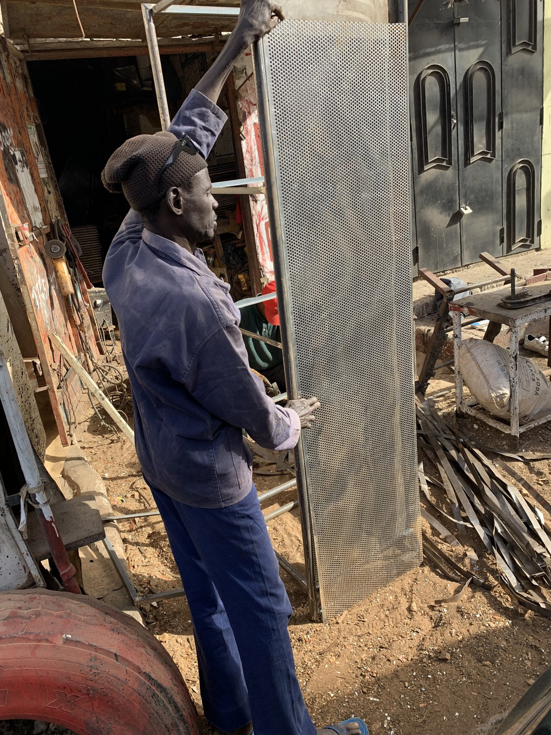 Baba, artisan du métal recyclé, manipulant un panneau métallique perforé dans son atelier dakarois.