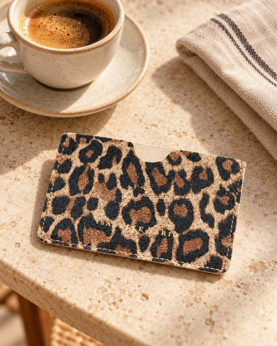 CREDY-Kartenetui von Isabelle Varin aus Leder mit Leopardenmuster, auf einem Cafétisch aus hellem Stein.