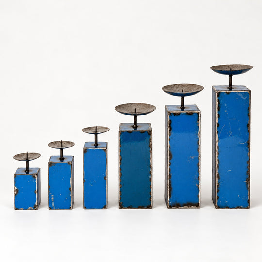 Les six tailles de bougeoirs NURU en métal recyclé bleu, alignées de la plus petite à la plus grande sur fond clair.