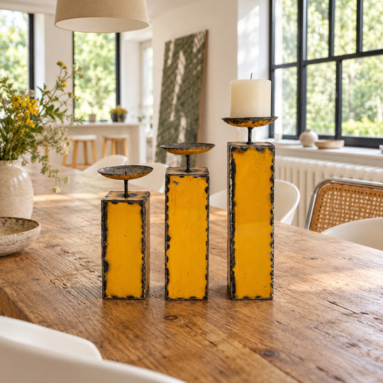 Trois bougeoirs NURU en métal recyclé jaune sur une table en bois dans une salle à manger lumineuse.