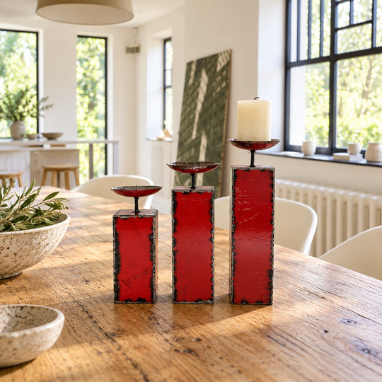 Trois bougeoirs NURU en métal recyclé rouge sur une table en bois dans une salle à manger lumineuse.