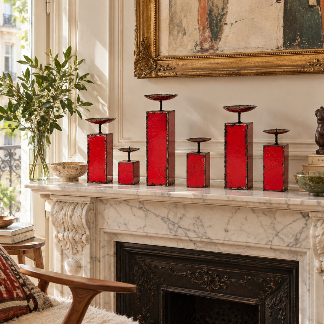 Six bougeoirs NURU rouges en métal recyclé, de tailles variées, disposés sur une cheminée haussmannienne en marbre clair.

