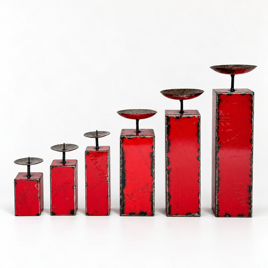 Les six tailles de bougeoirs NURU en métal recyclé rouge, alignées de la plus petite à la plus grande sur fond clair.