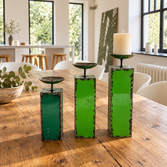 Trois bougeoirs NURU en métal recyclé vert sur une table en bois dans une salle à manger lumineuse.