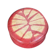 Boîte ronde en cuir rouge à motif rayonnant beige, fermée et vue de trois quarts sur fond blanc.