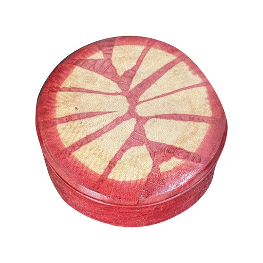 Boîte ronde en cuir rouge à motif rayonnant beige, fermée et vue de trois quarts sur fond blanc.