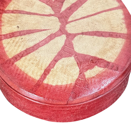 Gros plan sur le grain du cuir rouge et le motif rayonnant beige du couvercle de la boîte.
