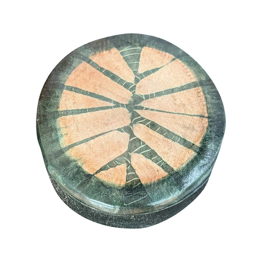 Boîte ronde en cuir vert foncé à motif rayonnant saumon, fermée et vue de trois quarts sur fond blanc.