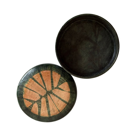 Boîte ronde en cuir vert foncé, ouverte sur un intérieur uni, avec son couvercle à motif rayonnant saumon à côté.