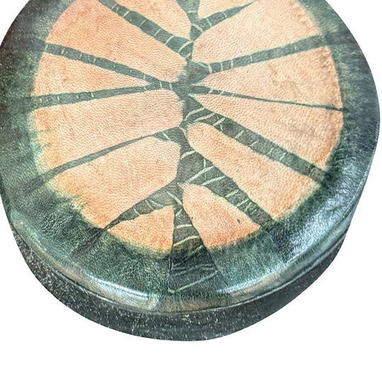 Gros plan sur le grain du cuir vert foncé et le motif rayonnant saumon du couvercle de la boîte.