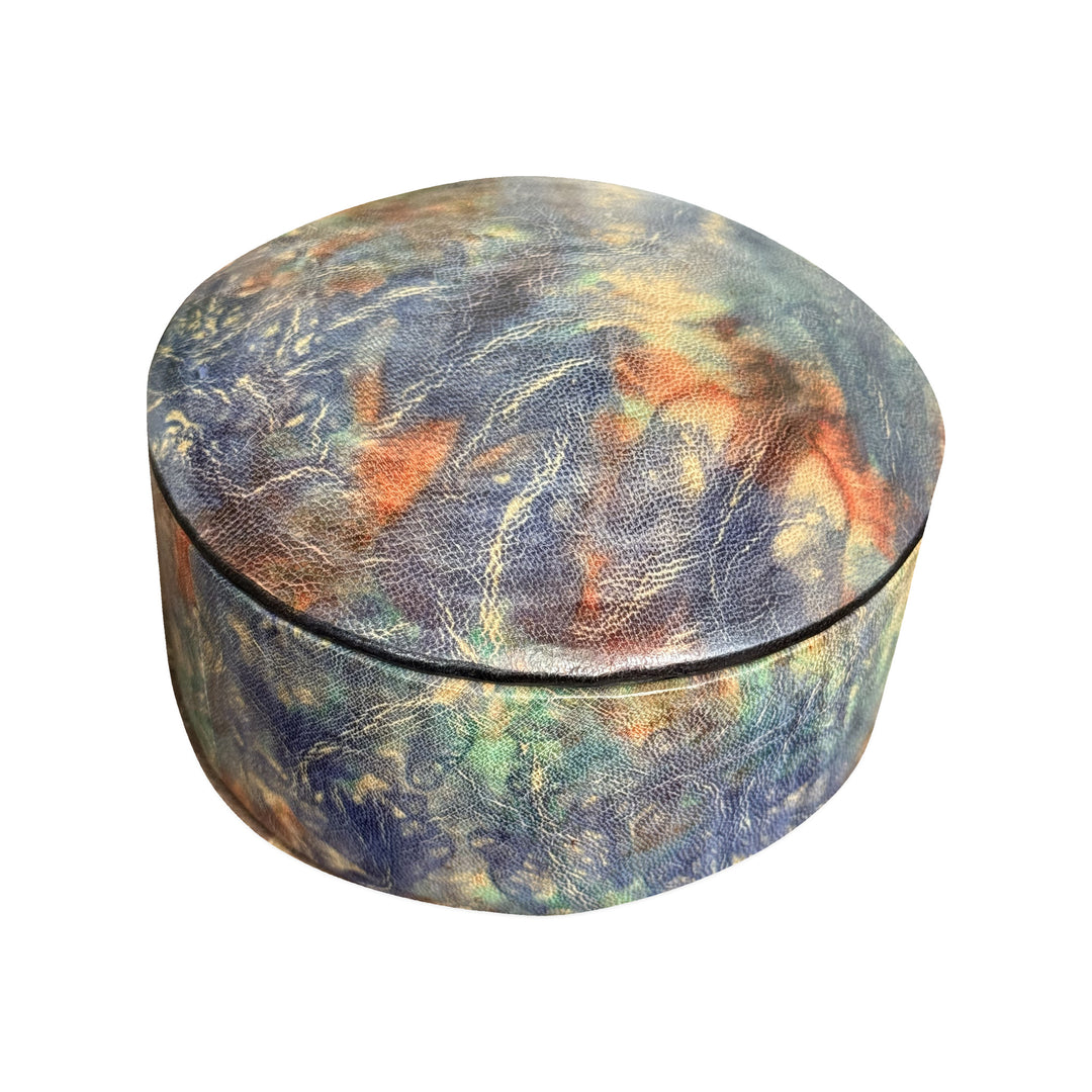 Boîte ronde en cuir marbré bleu, turquoise et orange, fermée et vue de trois quarts sur fond blanc.