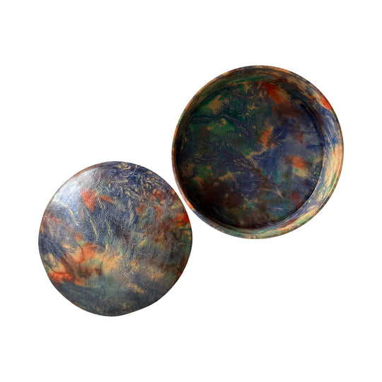 Boîte ronde en cuir marbré bleu, turquoise et orange, ouverte avec son couvercle posé à côté sur fond blanc.