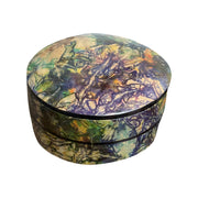 Boîte ronde en cuir marbré violet, vert et ocre, fermée et vue de trois quarts sur fond blanc.